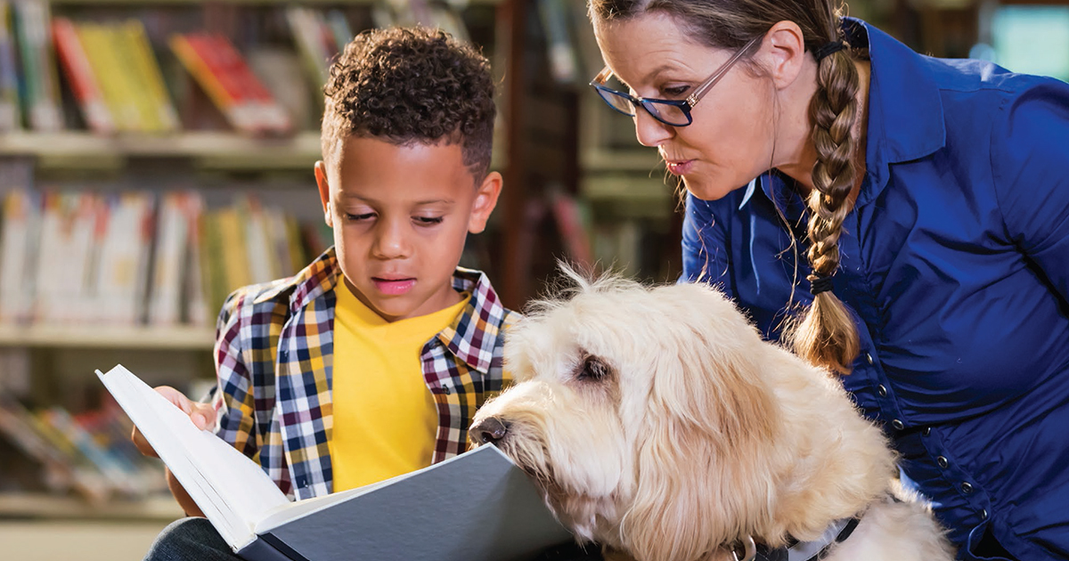 young boy and woman read a book with a white dog