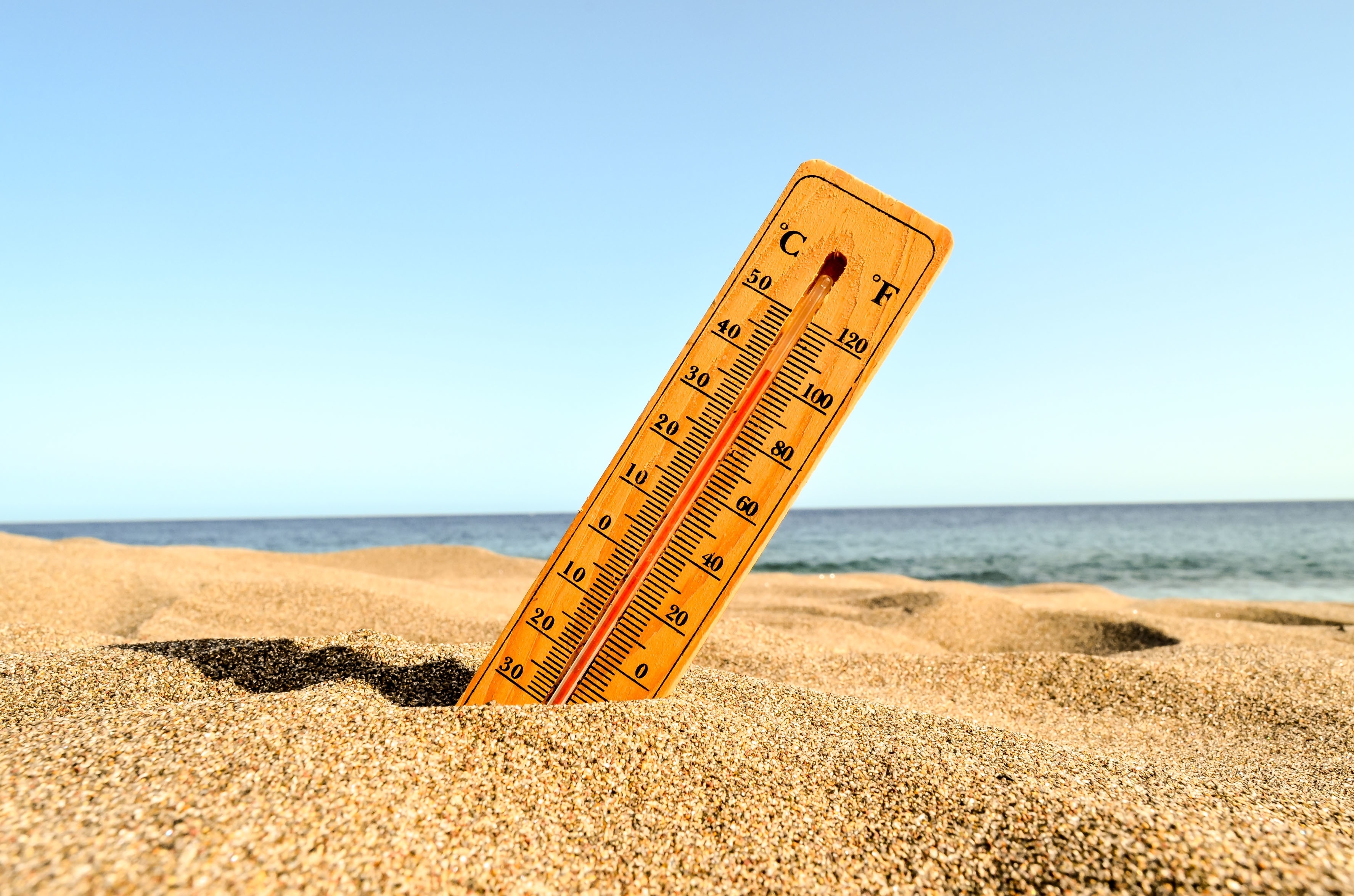 A thermometer stuck in the sand at a beach, displaying a high temperature reading on a clear sunny day, symbolizing a heatwave.